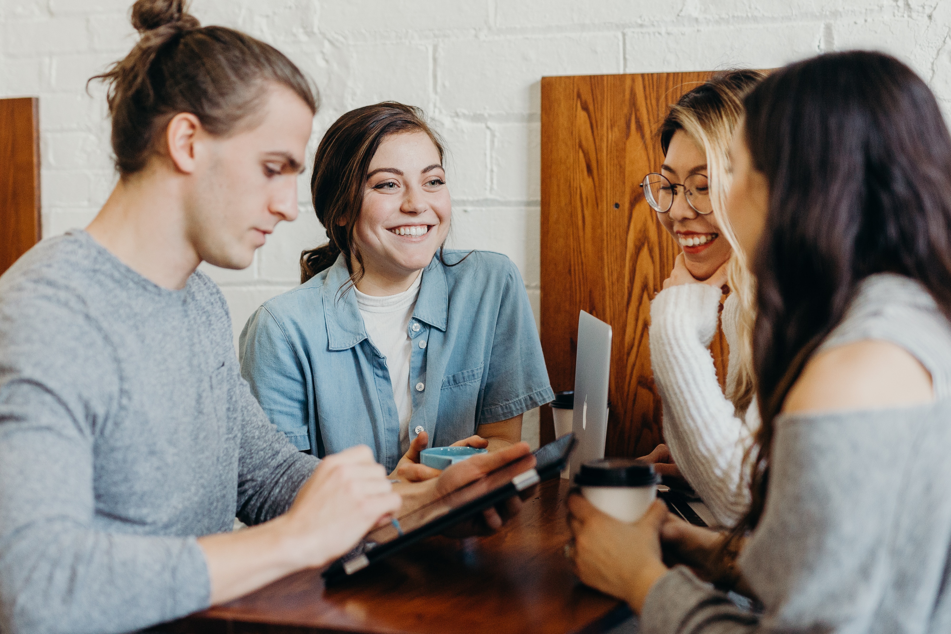 A group of four people smile and talk over a coffee and laptop