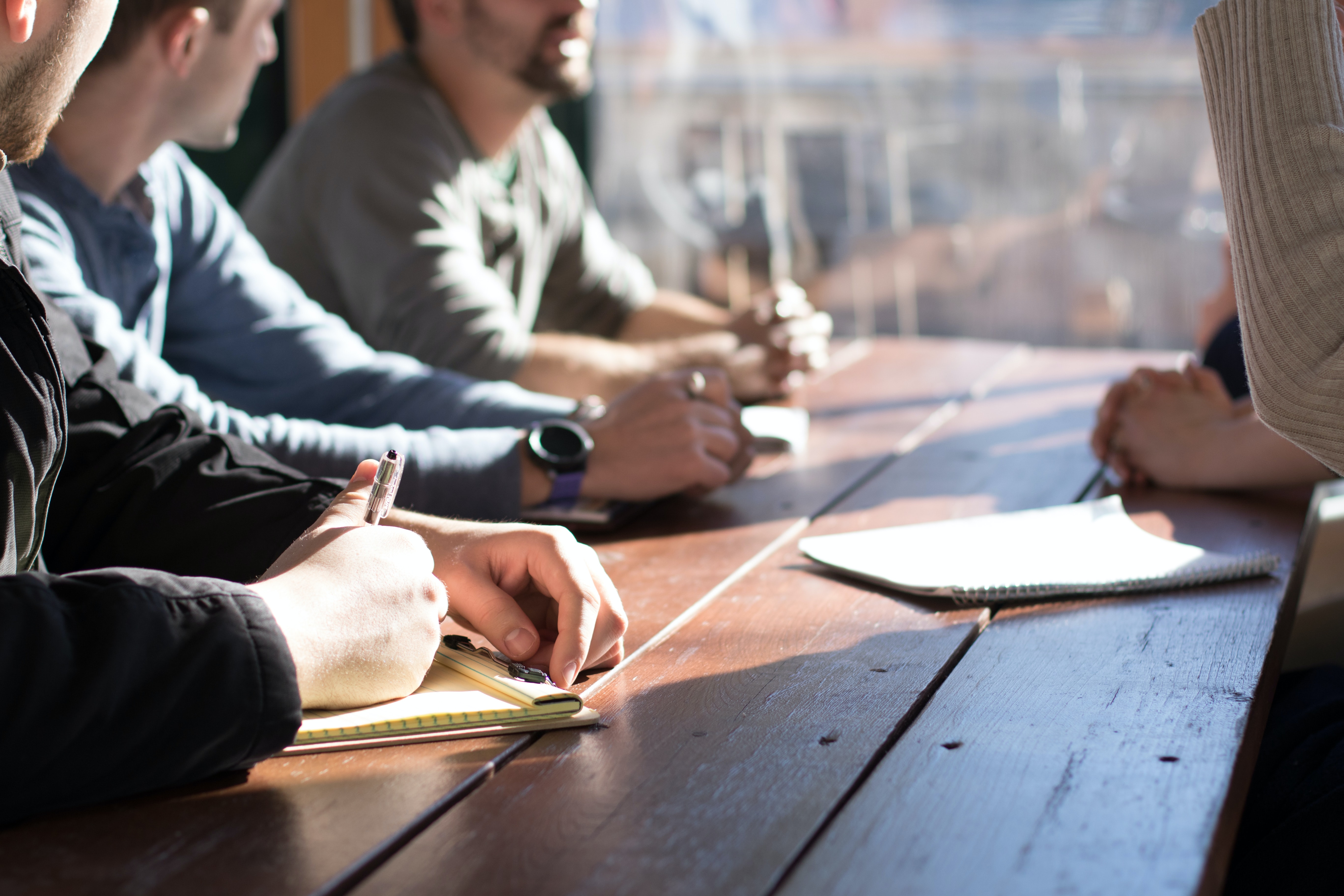 People sit around a table, talking and making notes on a notepad